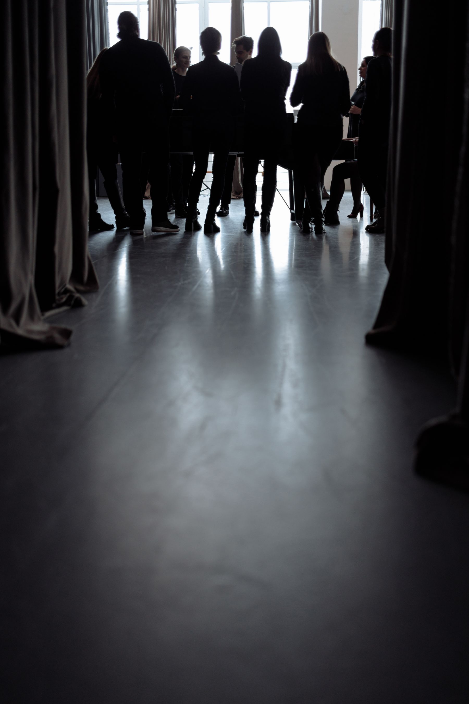 Silhouettes of a team gathered in conversation against tall backlit windows