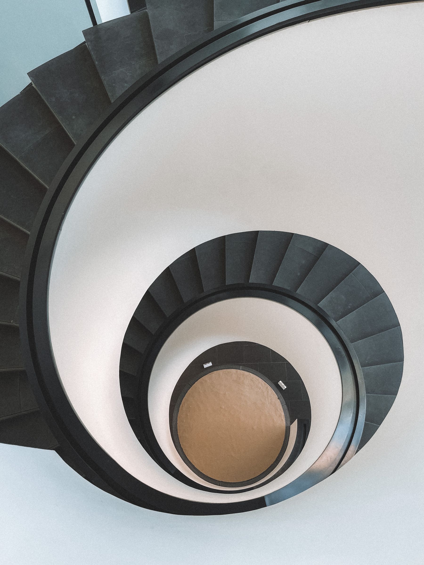 A spiral staircase seen from above, winding down to a small circle of light