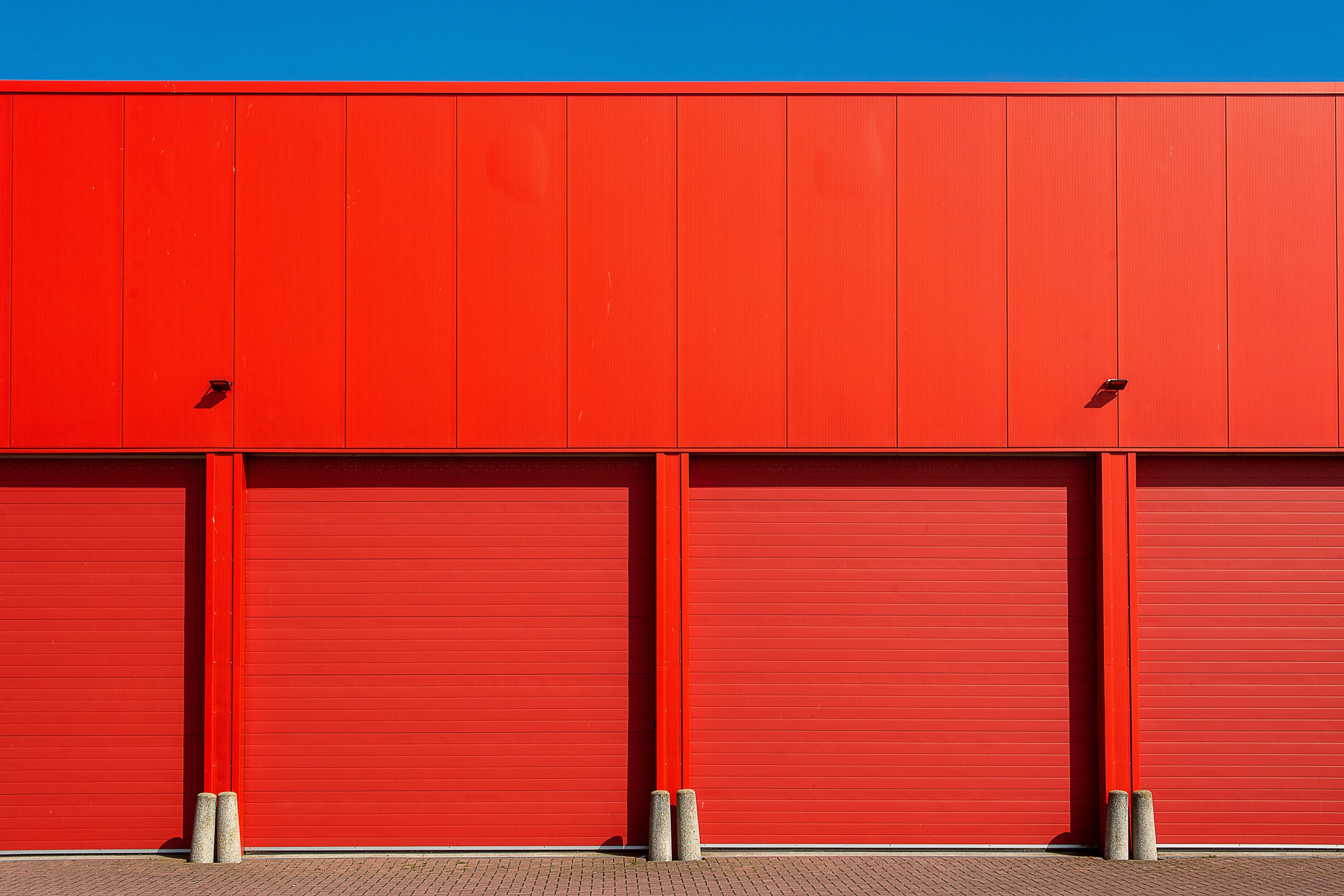 A bold red warehouse facade with roller doors under a blue sky