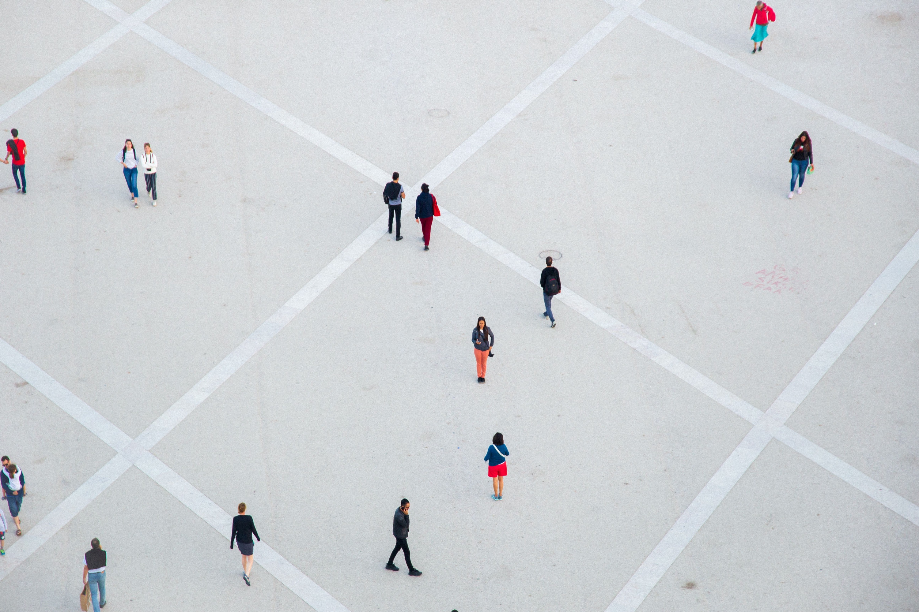 People walking across a large paved plaza, seen from above